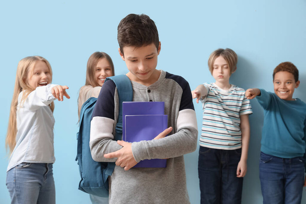 Gemobbter kleiner Junge mit Textbüchern und Schülern auf blauem Hintergrund - Foto, Bild