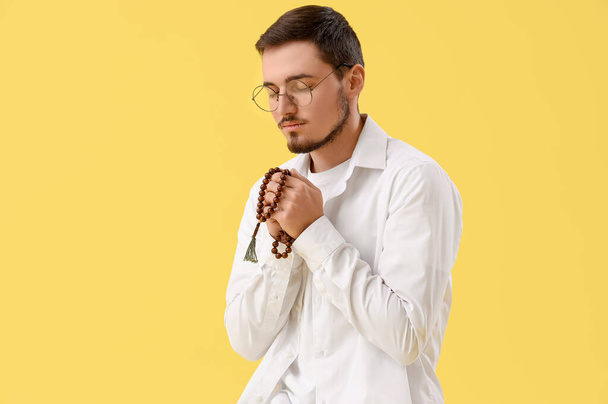Young man with rosary beads praying on yellow background - Photo, Image