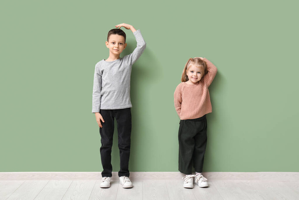 Niedliche kleine Kinder messen Höhe in der Nähe der grünen Mauer - Foto, Bild
