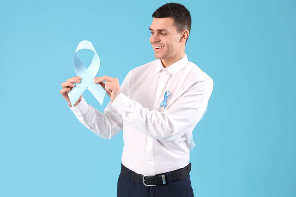 Молодой бизнесмен с голубыми лентами на цветном фоне. Концепция информирования о раке предстательной железы - Фото, изображение