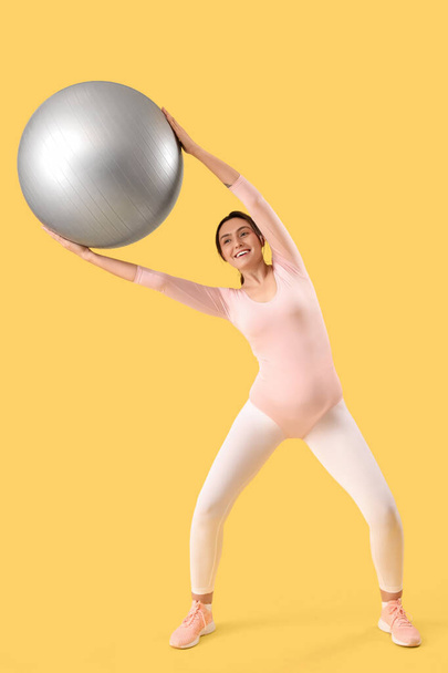 Happy young pregnant woman training with fitball on yellow background - Zdjęcie, obraz