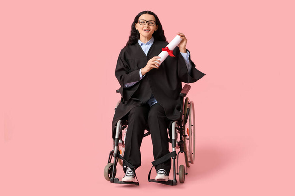 Krásná žena postgraduální student v invalidním vozíku s diplomem na růžovém pozadí - Fotografie, Obrázek
