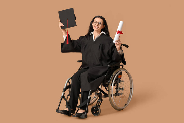 茶色の背景で卒業キャップと卒業証書を持つ車椅子の美しい女性の大学院生 - 写真・画像