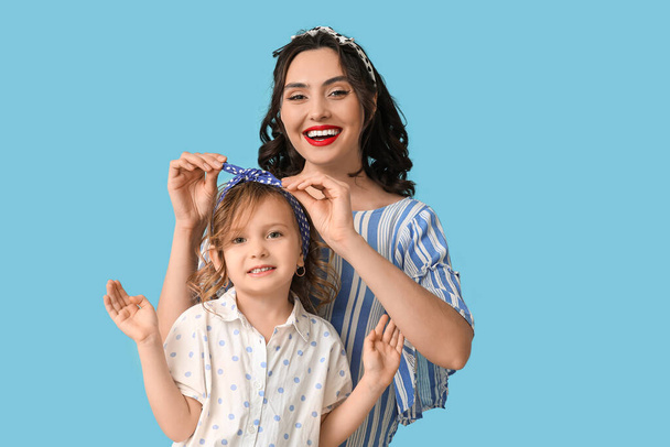 Beautiful pin-up woman and her daughter on blue background - Photo, Image