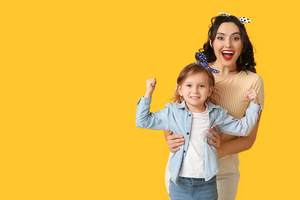 Όμορφη γυναίκα pin-up και η κόρη της δείχνει μυς σε κίτρινο φόντο - Φωτογραφία, εικόνα