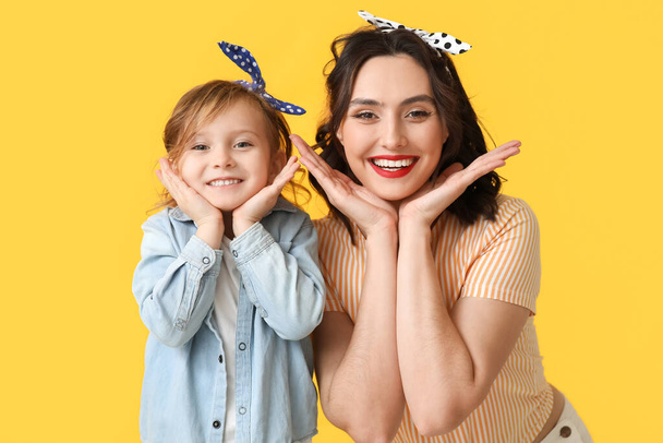 Happy pin-up woman and her daughter on yellow background - Photo, Image