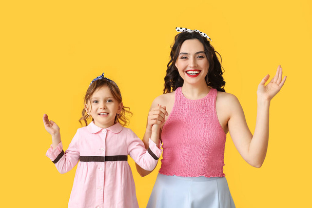 Happy pin-up woman and her daughter on yellow background - Photo, Image