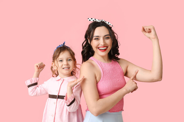 Beautiful pin-up woman and her daughter showing muscles on pink background - Photo, Image