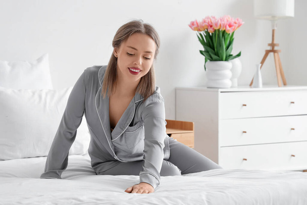 Kaunis nuori nainen pyjamassa petaus sängyssä makuuhuoneessa - Valokuva, kuva