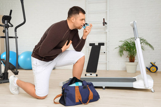 Sporty young man with bag using inhaler in gym - Photo, Image