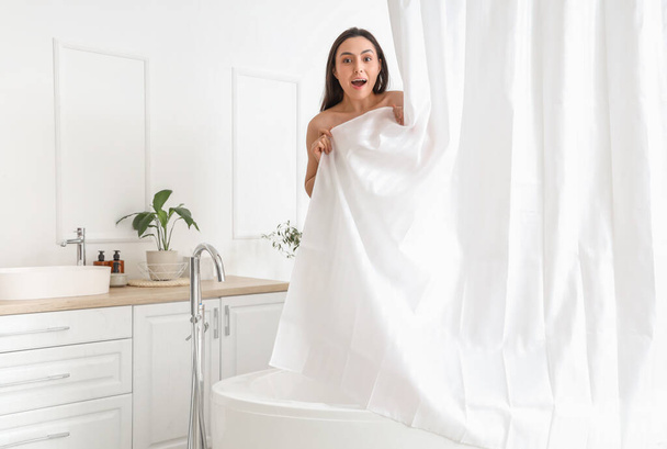 Удивлённая молодая женщина за занавесом принимает ванну дома - Фото, изображение