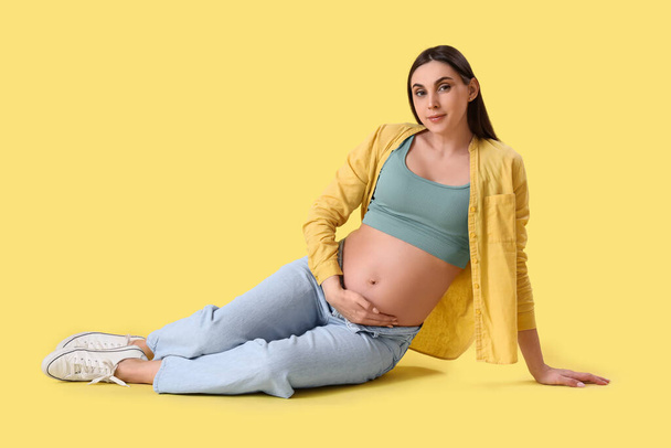 Jonge zwangere vrouw zittend op gele achtergrond - Foto, afbeelding