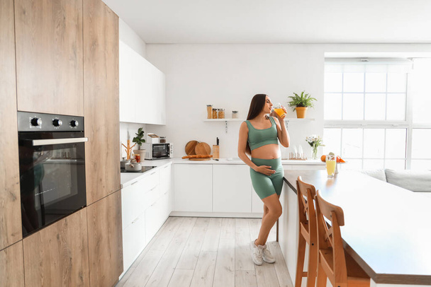 Femme enceinte sportive buvant du jus dans la cuisine - Photo, image