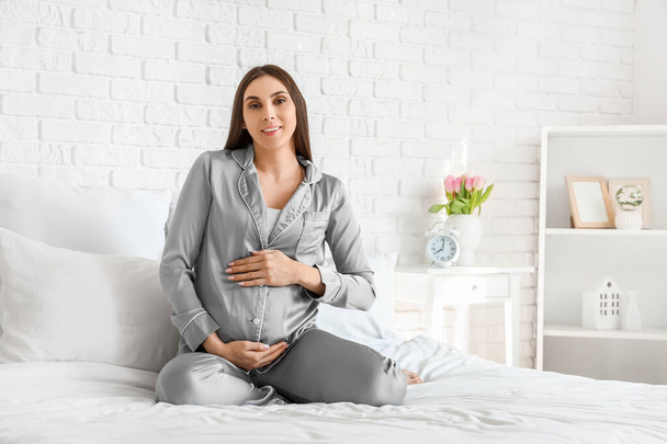 Молода вагітна жінка сидить у спальні
 - Фото, зображення