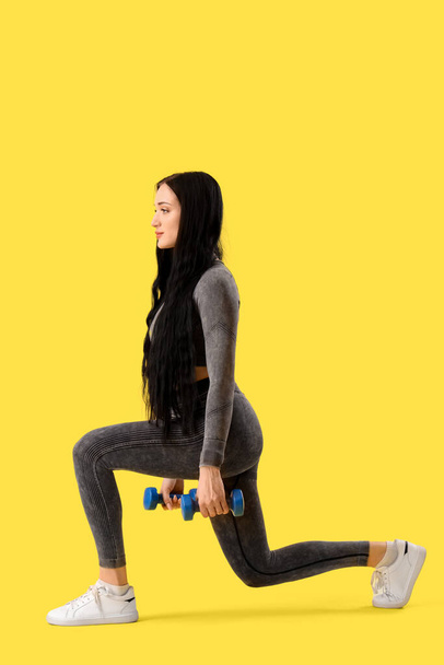 Portrait of sporty young woman exercising with dumbbells on yellow background - Photo, Image