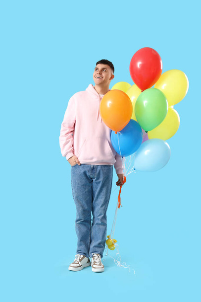 Young man with bunch of colorful balloons on blue background - Photo, Image