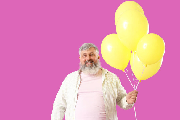 Senior férfi egy csomó sárga lufi rózsaszín háttér - Fotó, kép