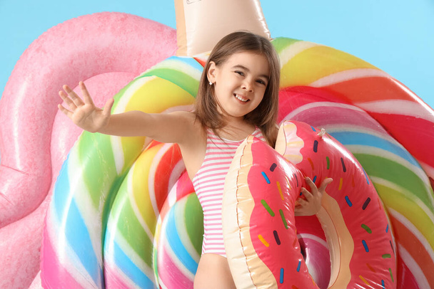 Cute little girl with inflatable ring in shape of donut and mattresses on blue background - Photo, Image