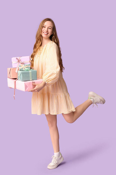 Glückliche junge Frau mit Geschenkboxen auf fliederfarbenem Hintergrund - Foto, Bild