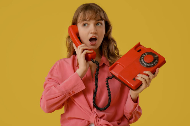 jong verrast vrouw praten met retro telefoon op gele achtergrond - Foto, afbeelding