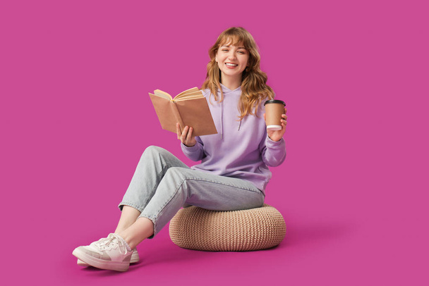 Mutlu genç kadın kitap okuyor ve mor arka planda kahve içiyor. - Fotoğraf, Görsel