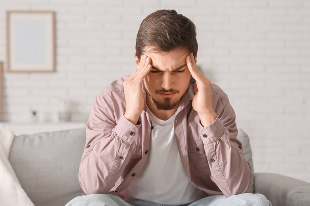 Unavený mladý muž s bolestí hlavy sedí doma na pohovce - Fotografie, Obrázek