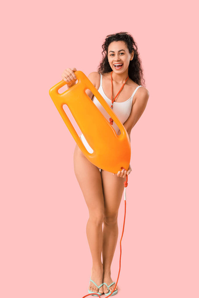 Schöne junge glückliche afroamerikanische Rettungsschwimmerin mit Rettungsboje auf rosa Hintergrund - Foto, Bild