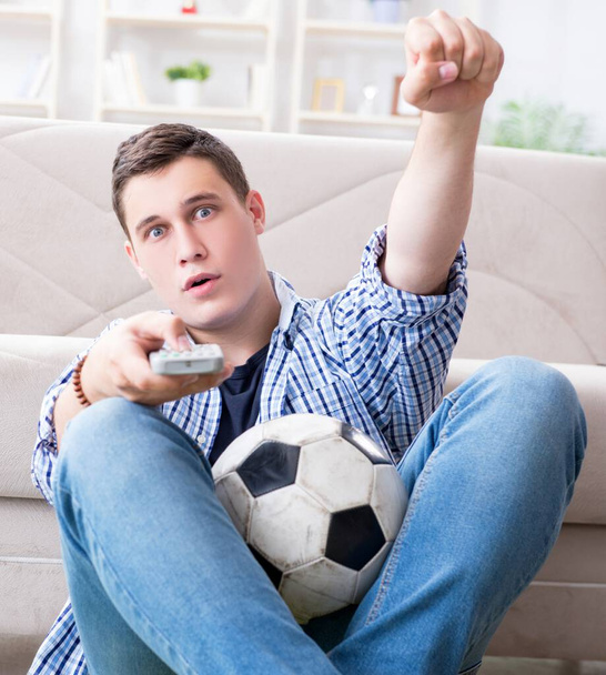 Молодой человек смотрит футбол дома - Фото, изображение