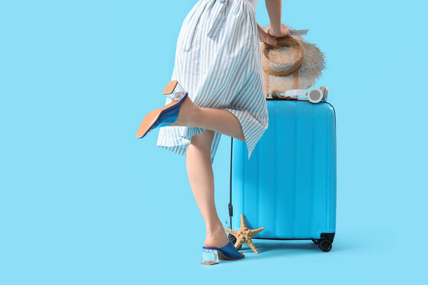 Női utazó bőrönddel és strand tartozékok kék háttér - Fotó, kép