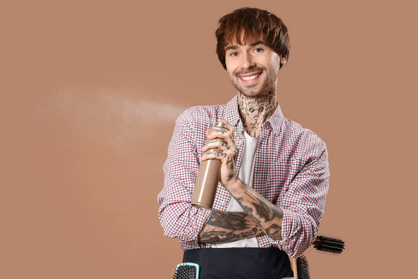 Tattooed barber with hair spray on brown background - Photo, Image