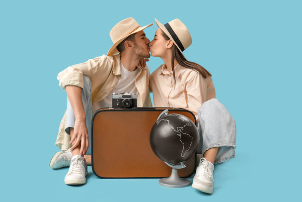 Hermosa joven feliz pareja de turistas con maleta, cámara y globo besos sobre fondo azul - Foto, imagen
