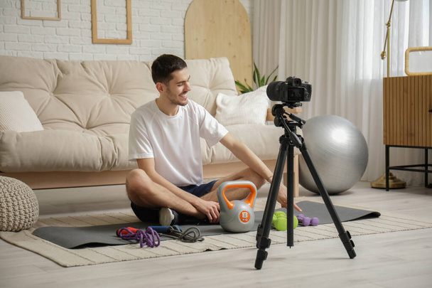 Deportivo feliz blogger masculino con pesas, saltar cuerdas y kettlebell grabación de vídeo en casa - Foto, imagen