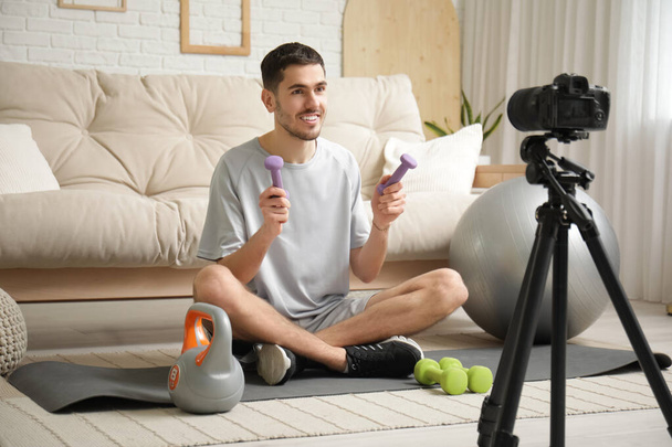 自宅でビデオを録画するダンベルとケトルベルを持つスポーティ幸せな男性ブロガー - 写真・画像