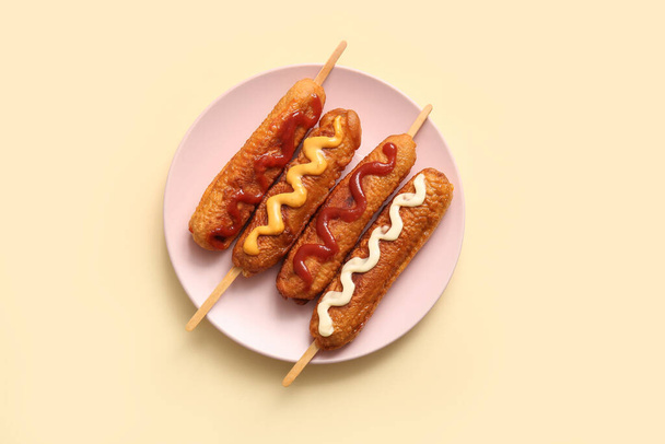 Assiette de savoureux chiens de maïs avec différentes sauces sur fond jaune - Photo, image