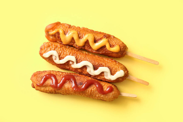 Smaczne hot dogi kukurydziane z różnymi sosami na żółtym tle - Zdjęcie, obraz