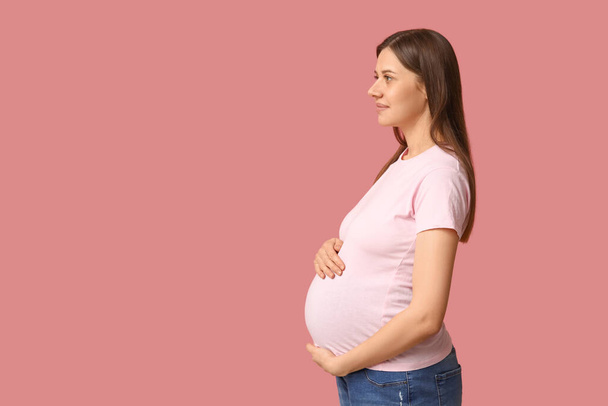 Schöne junge schwangere Frau in stylischem T-Shirt auf rosa Hintergrund - Foto, Bild