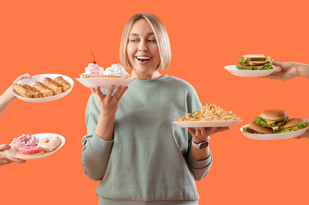 Beautiful woman and hands with unhealthy food on orange background. Overeating concept - Photo, Image