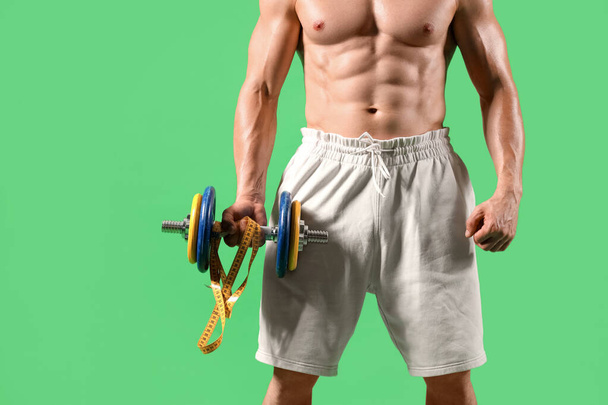 bodybuilder masculin avec ruban à mesurer et haltère sur fond vert - Photo, image
