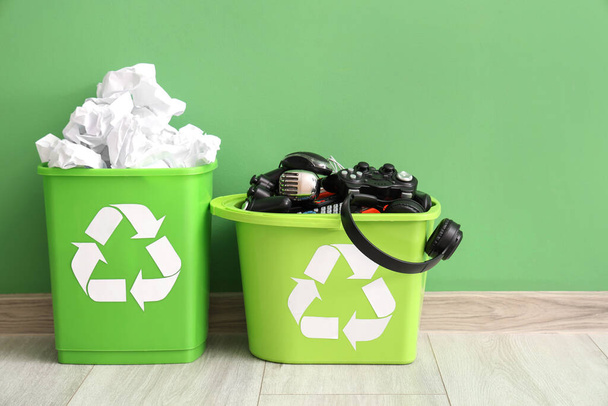 Papeleras de reciclaje con papel y electrónica cerca de la pared verde. Concepto de reciclaje - Foto, imagen
