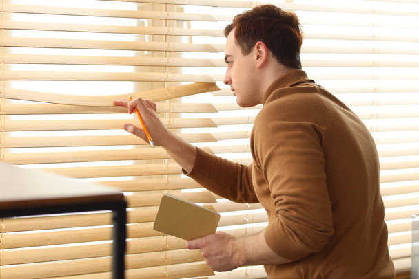 Männlicher Spion mit Notizbuch schaut aus Fenster im Büro - Foto, Bild