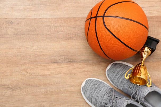 Ball voor het spelen van basketbal, beker en schoenen op houten achtergrond, close-up - Foto, afbeelding