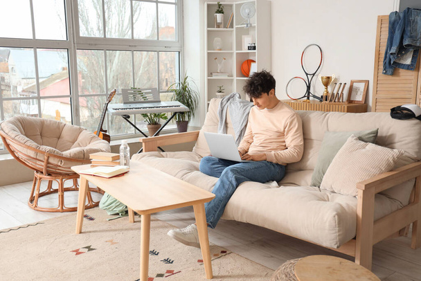 Чоловік студент використовує ноутбук на дивані вдома - Фото, зображення