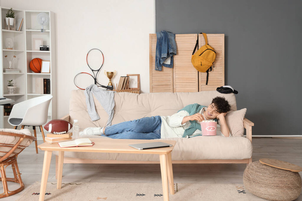 Άνδρας φοιτητής με ποπ κορν βλέποντας τηλεόραση στον καναπέ στο σπίτι - Φωτογραφία, εικόνα