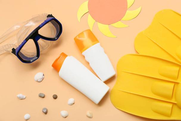 Flessen zonnebrandcrème, duikmasker en flippers op oranje achtergrond - Foto, afbeelding