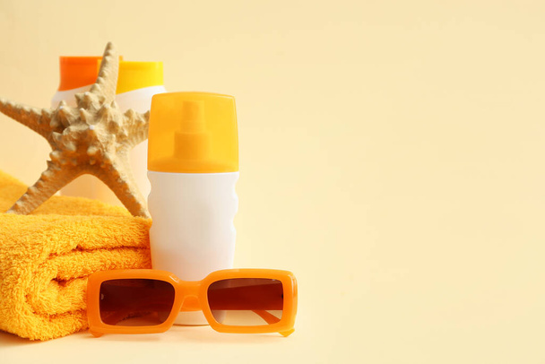 Flaschen Sonnencreme, Seesterne, Handtuch und Sonnenbrille auf beigem Hintergrund - Foto, Bild