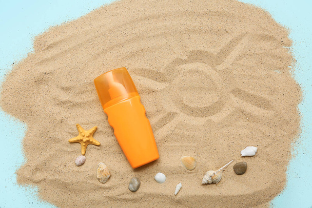 Fles zonnebrandcrème, schelpen en zand op blauwe achtergrond - Foto, afbeelding