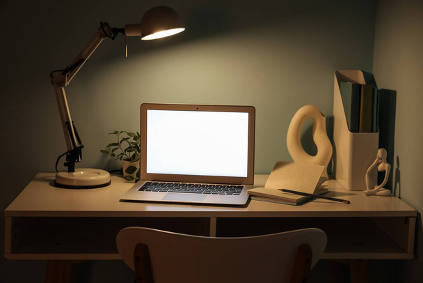 Local de trabalho com laptop moderno, estatueta e lâmpada brilhante perto da parede verde - Foto, Imagem