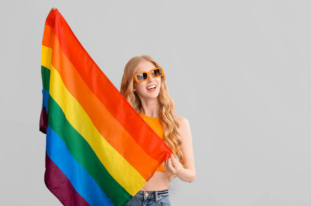 Hermosa joven feliz mujer con bandera LGBT sobre fondo gris - Foto, Imagen
