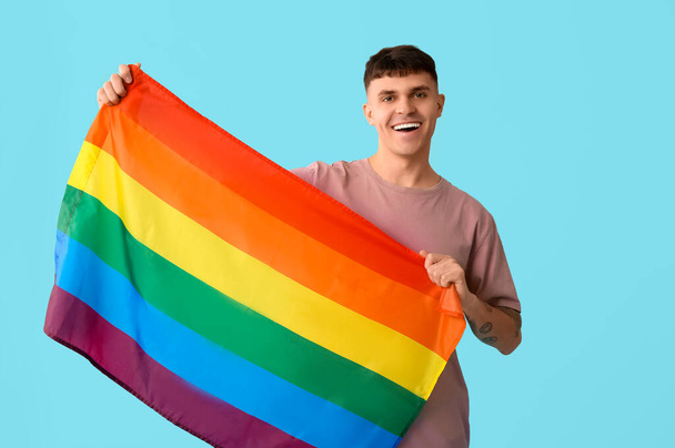 Schöner junger glücklicher Mann mit LGBT-Flagge auf blauem Hintergrund - Foto, Bild