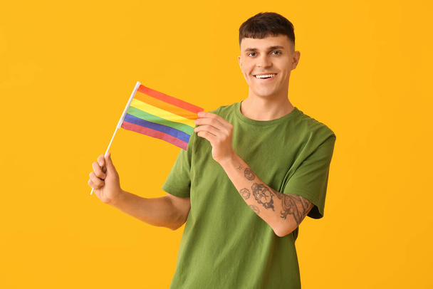 Guapo joven feliz hombre con bandera LGBT sobre fondo amarillo - Foto, imagen